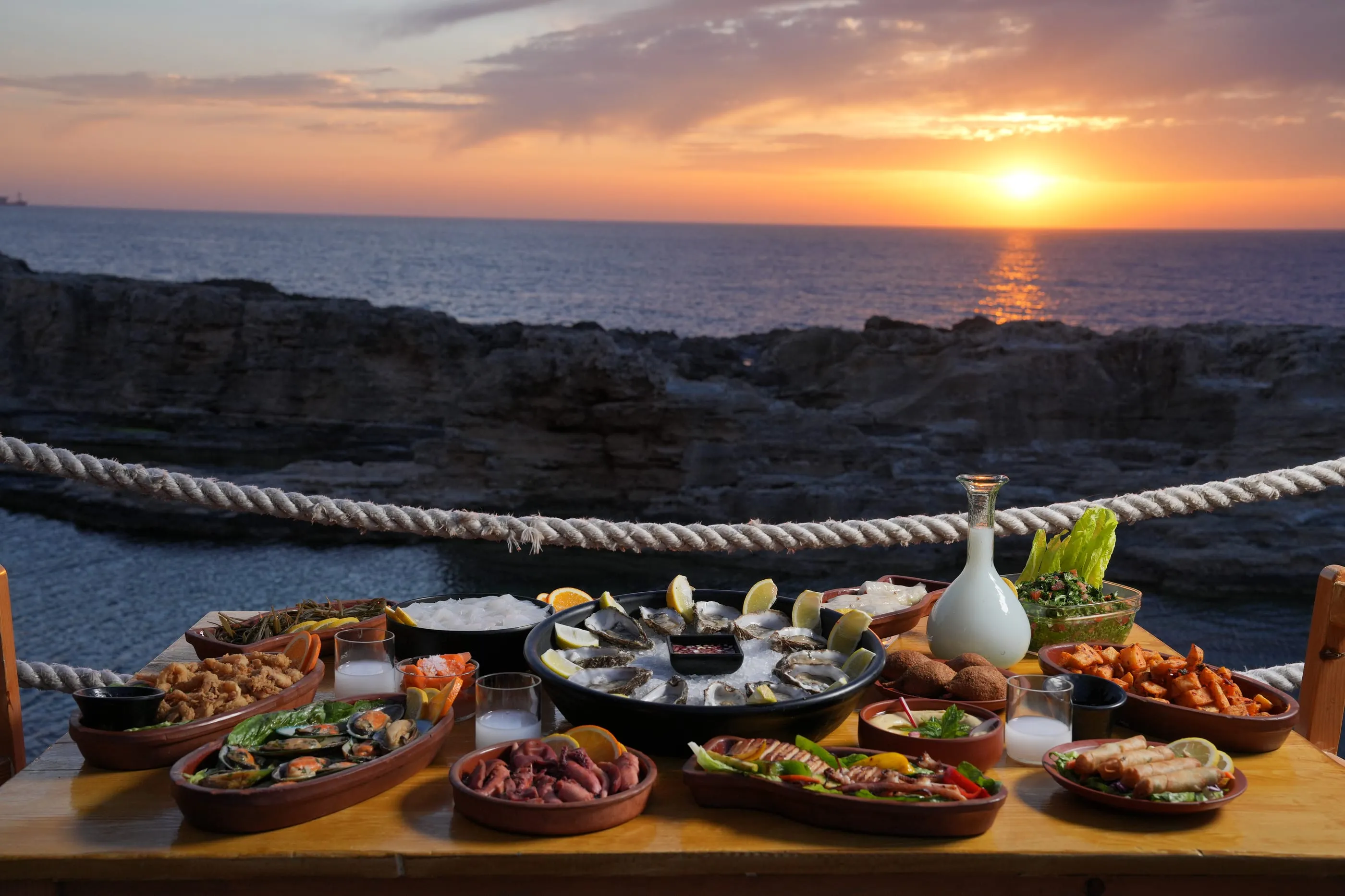 The sun going down over the sea behind a table of seafood at Batroun Mina, Oyster's Seafood Bar