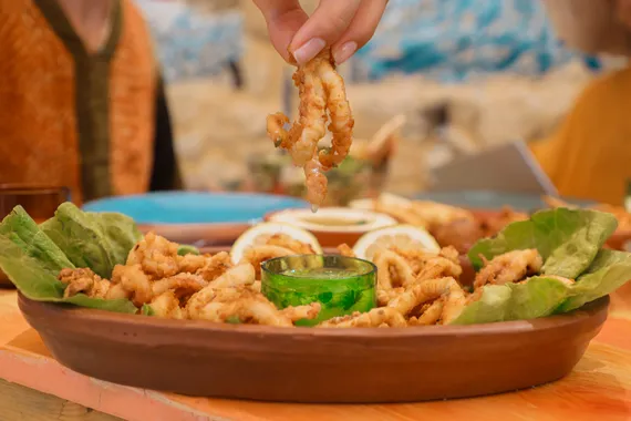 A hand lifting a piece of fried calamari from a terracotta dish at Oyster's Seafood Bar, Batroun