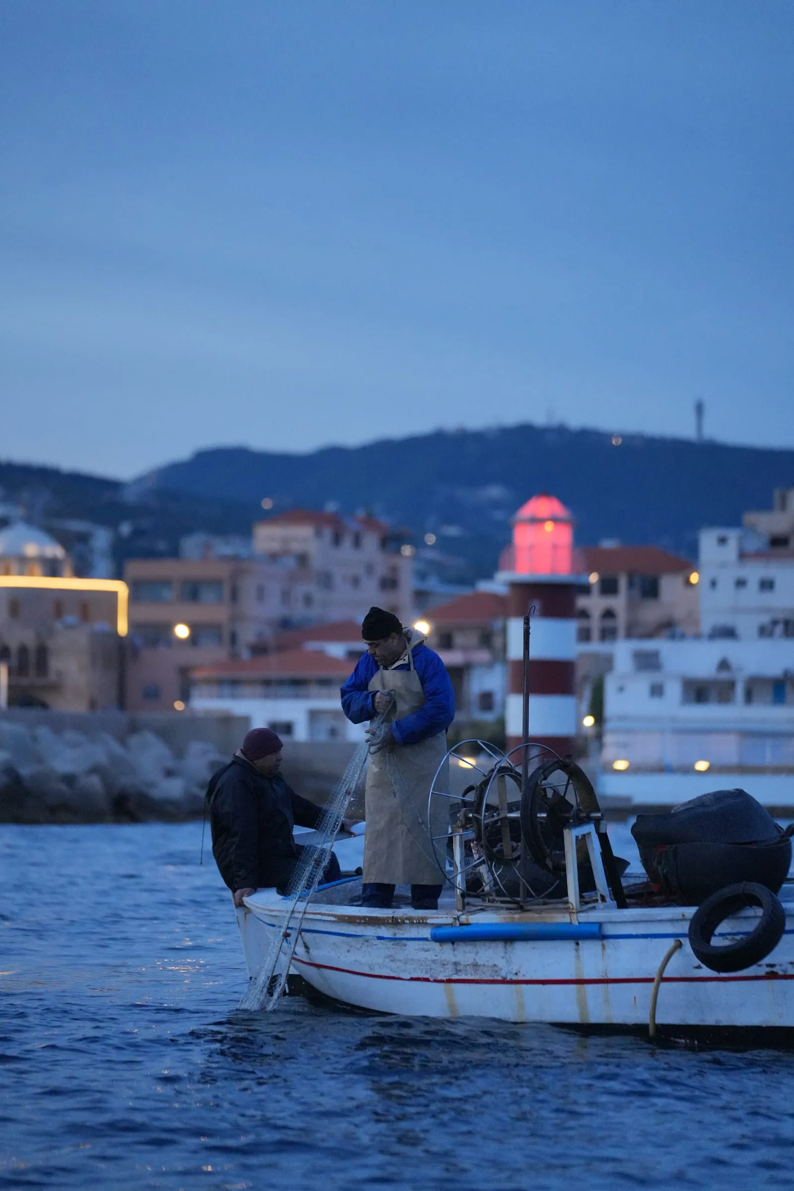 A fisherman in his boat at dusk at Batroun Mina, the red lighthouse behind