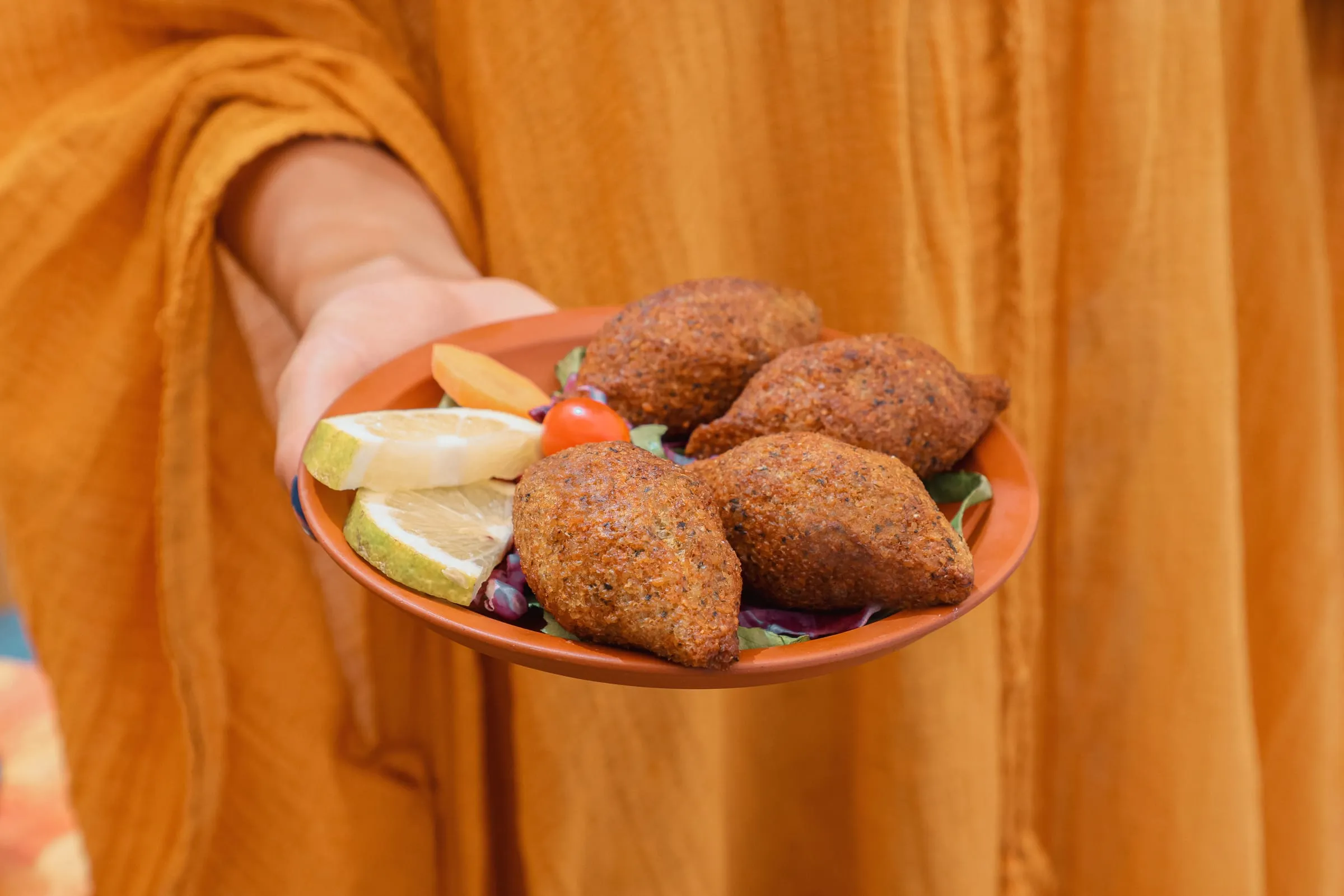 Four fish kebbe with lemon on a terracotta plate, held out across the table at Oyster's Seafood Bar, Batroun