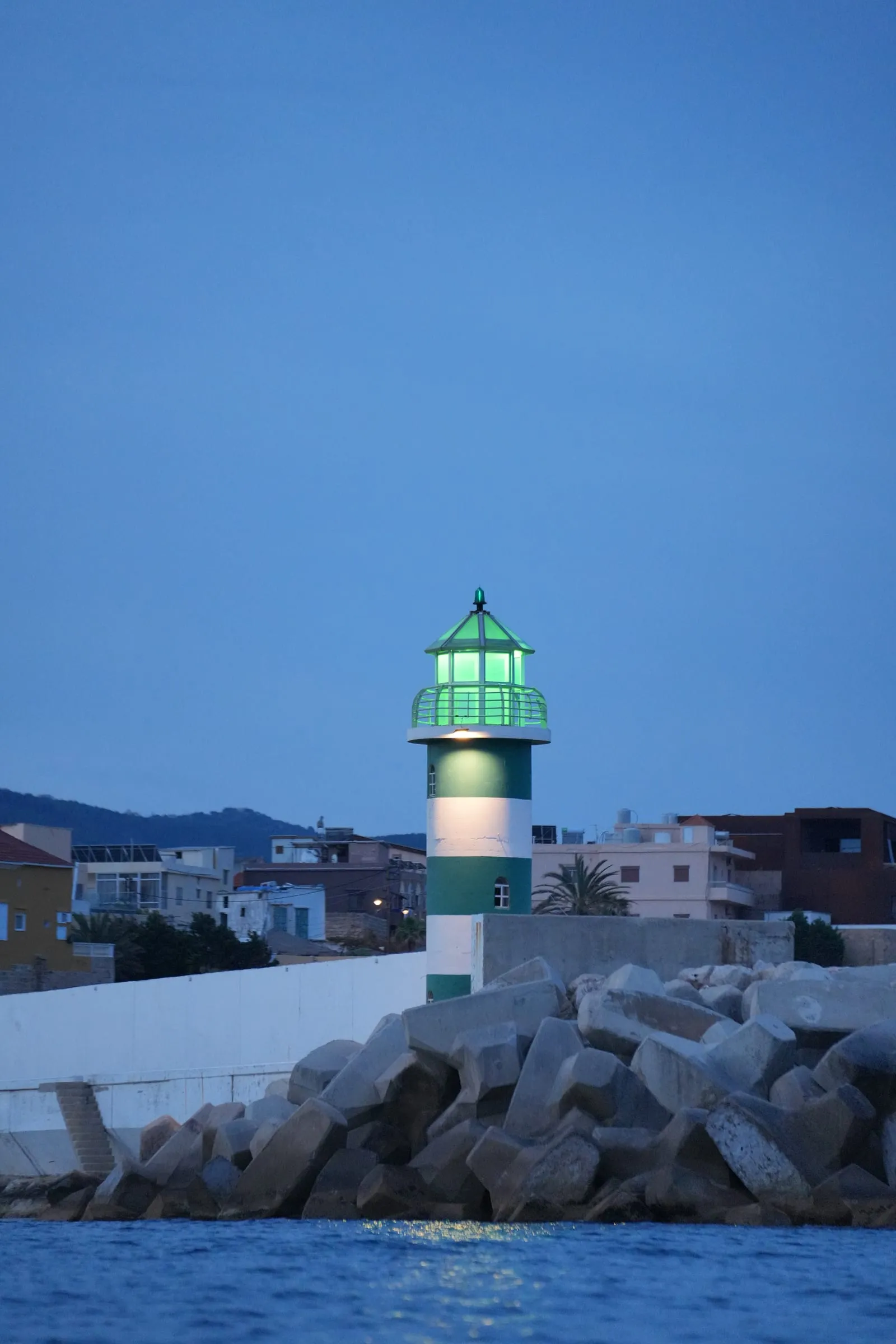 The green-lit lighthouse and breakwater of Batroun Mina at dusk, the fishermen's port where Oyster's Seafood Bar stands