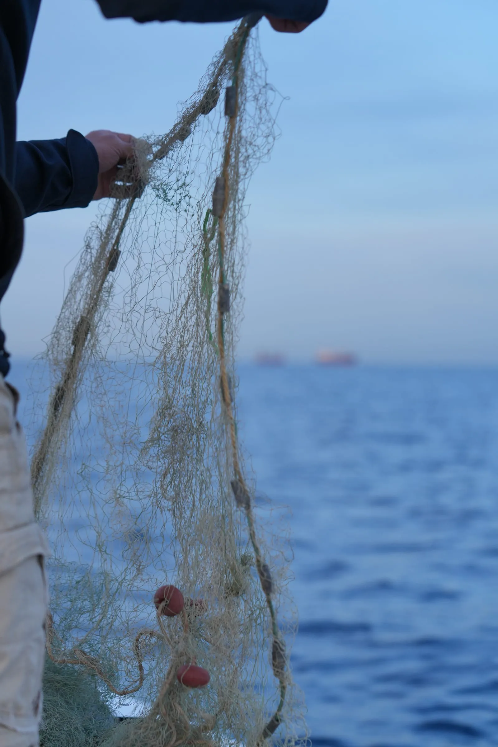 A hand holding a fishing net over the open sea off Batroun
