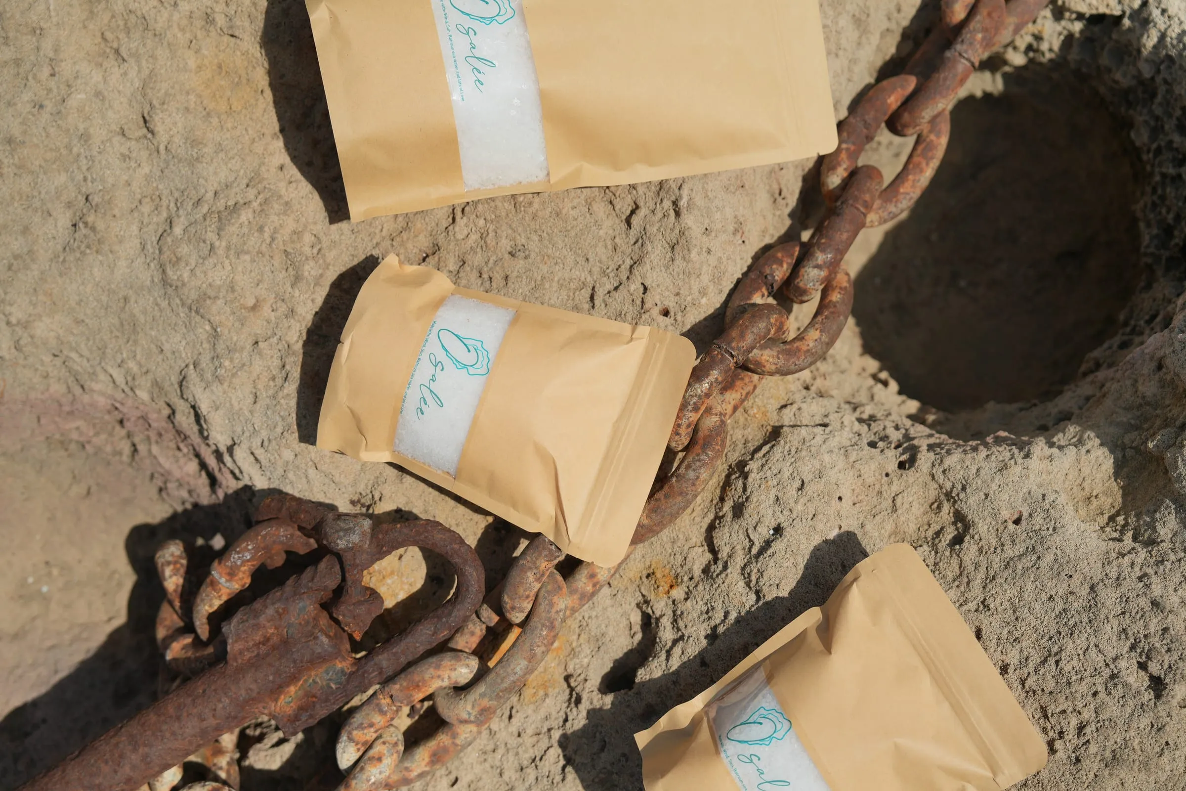 Kraft Osalée sea salt pouches on the rock beside a rusted chain, Batroun