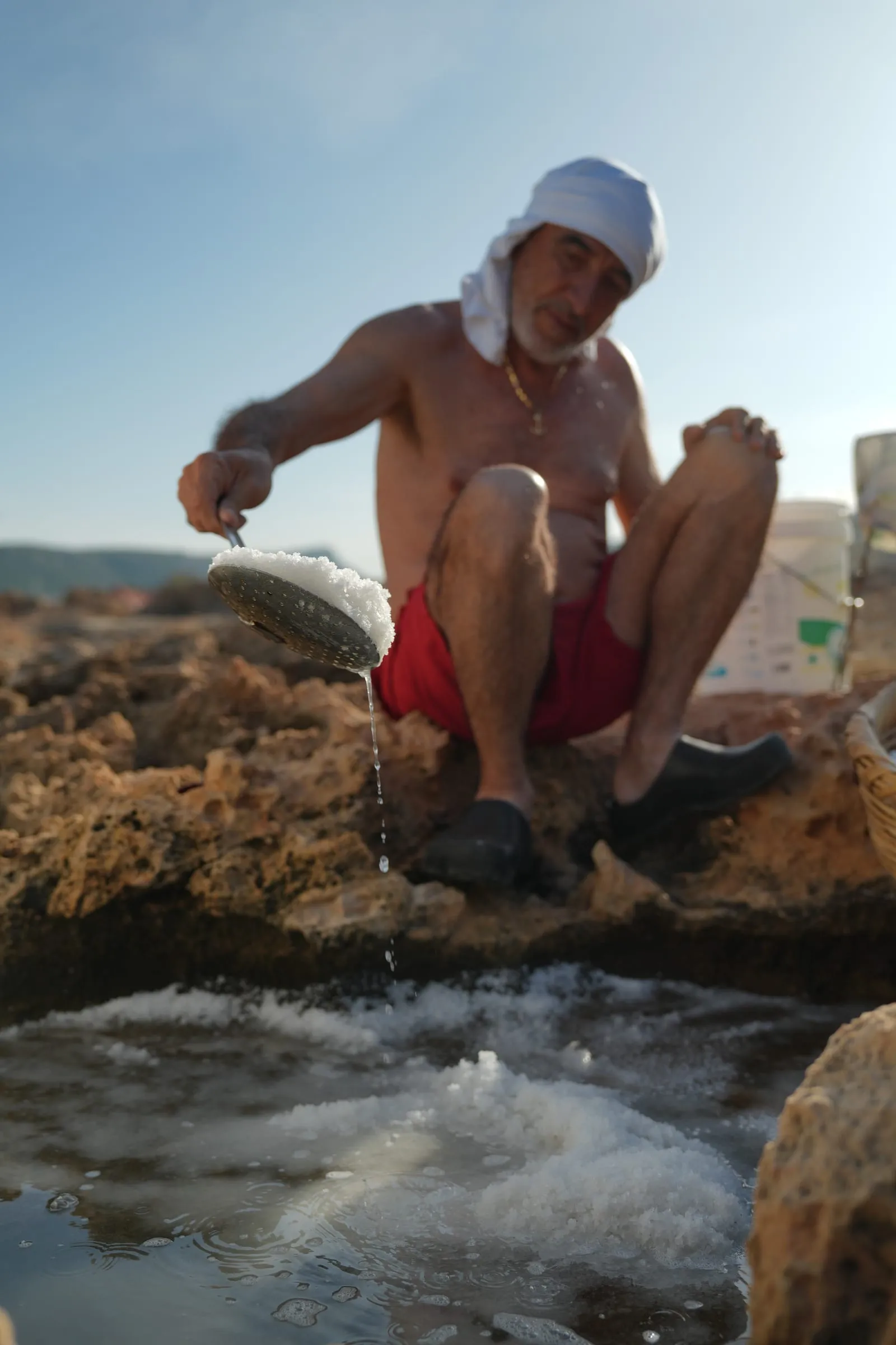 Our father, Assal, scooping sea salt from a rock pool at the Phoenician Wall salt ponds, Batroun