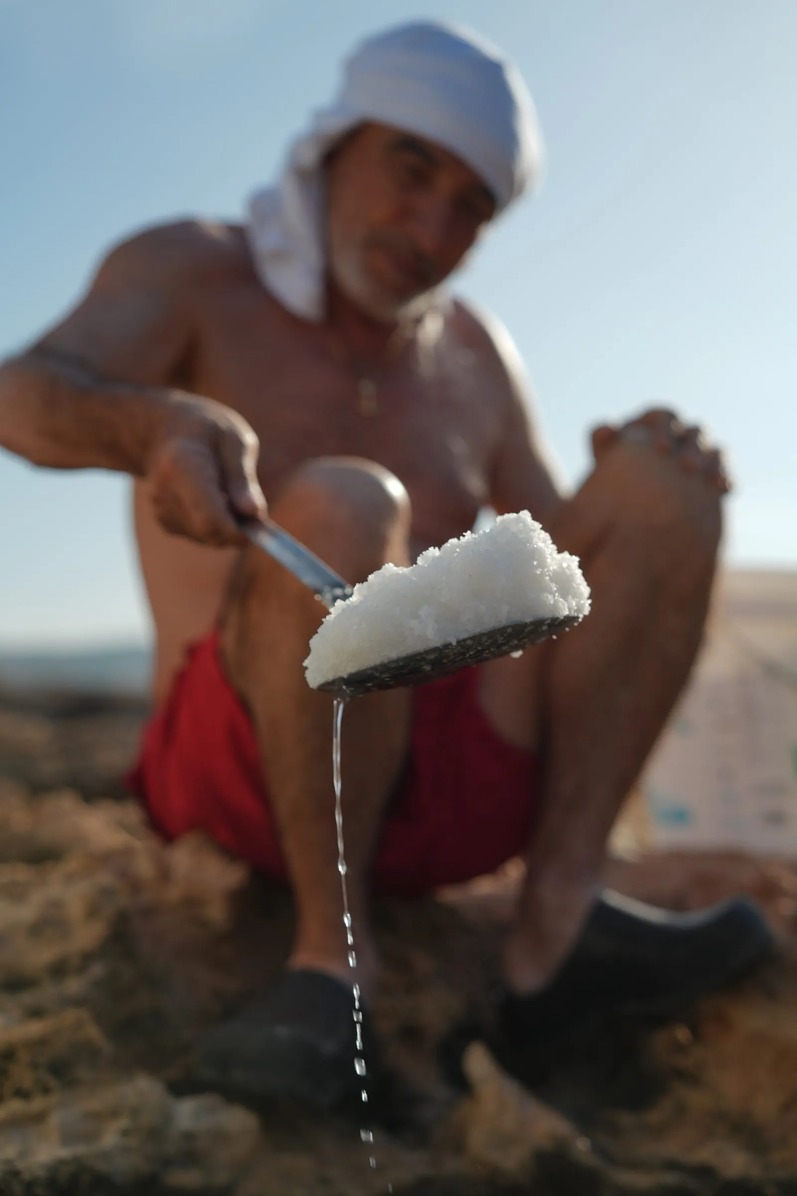 A sieve of wet sea salt crystals held over a rock pool at the Phoenician Wall salt ponds, Batroun