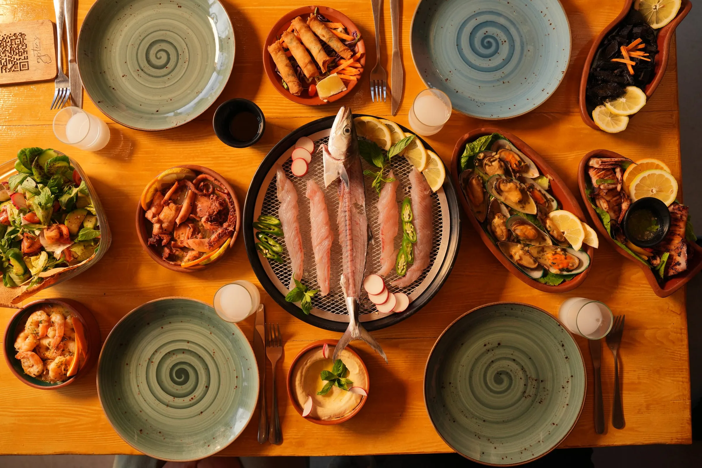 A table seen from above: a fish platter in the middle, mussels, salad, shrimp and plates set around it